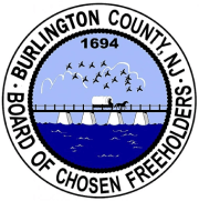 Seal of Burlington County, NJ. Image includes a covered wagon drawn by horses crossing a bridge over water, with flying birds and mountains in the background. Text reads "Burlington County, NJ. Board of Chosen Freeholders. 1694". Discover quality adult day care in Burlington County NJ for your loved ones.